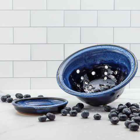 Dark blue ceramic colander next to blueberries on a kitchen counter
