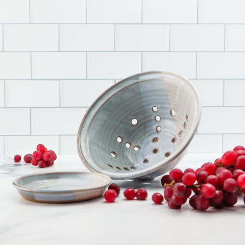 Off white ceramic colander next to red grapes on kitchen counter