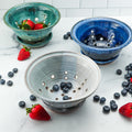 Strawberries and blueberries inside ceramic colanders